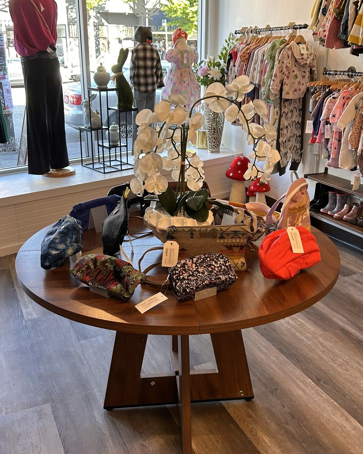 Inside The Clothes Nest — bags on the centre table, children's rail behind, Main Street through the window.